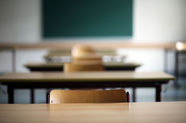 A stock image of an empty classroom's desks (focused on a desk in the foreground)